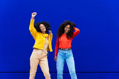 Young woman with arms raised standing against blue wall