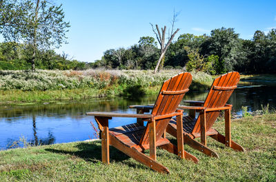 Empty chairs and table by lake against sky