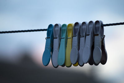 Close-up of clothespins hanging on rope against sky