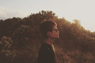 Side view of young man looking away against trees