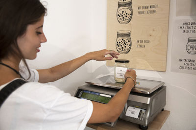 Young woman in packaging-free supermarket weighing goods on scale