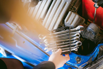 Cropped hand of man holding wrenches by car