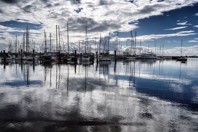 Boats in harbor against cloudy sky