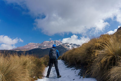 Rear view of man walking on snow covered mountain against sky