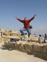 Cheerful man jumping from retaining wall against sky