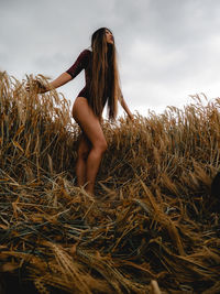 Low angle view of young woman standing on field against sky