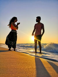 Full length of friends standing on beach against sky during sunset