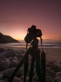 Silhouette dslr camera against sky on beach during sunset