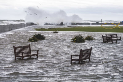 Empty chairs by sea against sky