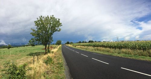 Road passing through field against cloudy sky