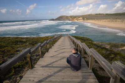 Man on footbridge over sea against sky