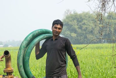 Portrait of young man holding water pipe standing at farm