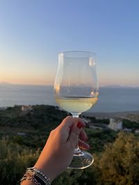 Cropped hand holding drink in glass against clear sky