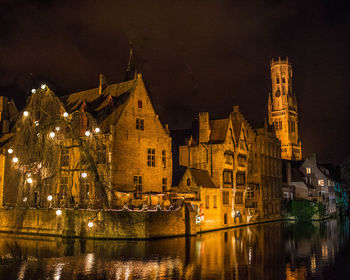 Illuminated buildings by river against sky in city at night