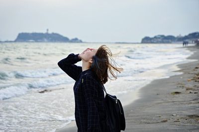 Young woman standing at beach against clear sky