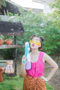Young woman holding squirt gun while standing in yard
