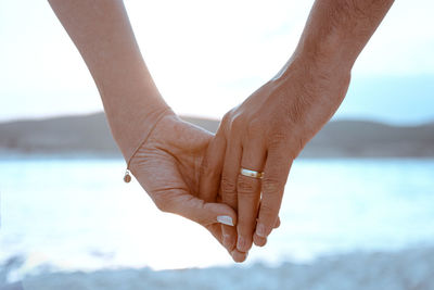 Close-up of hand holding hands against sky