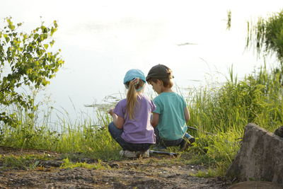 Rear view of siblings crouching at lakeshore