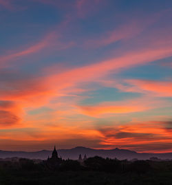 Silhouette temple by building against orange sky