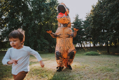 Person wearing dinosaur costume chasing boy in park