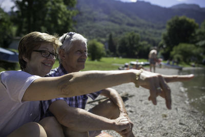 Senior woman pointing to husband while sitting at kochelsee lakeshore