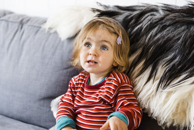 Cute girl looking away while sitting on sofa at home