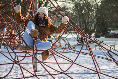 Full length of woman climbing on ropes at snow covered park