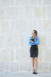 Full length of young woman standing in front of wall