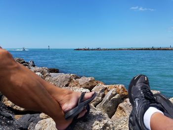 Low section of people on rock by sea against clear sky