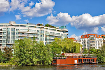 Ferry boat in river by buildings against sky