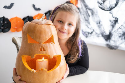 Cute girl in costume of witch with pumpkin at home, having fun, celebrating halloween