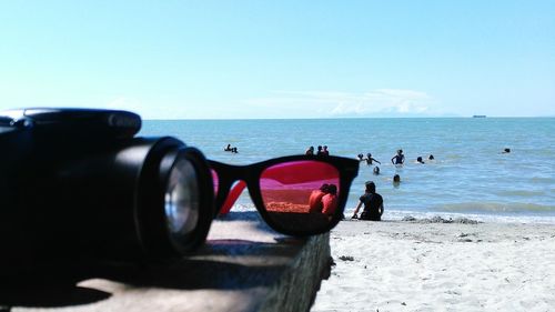 Close-up of sunglasses on beach against clear sky