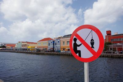 Information sign by river against sky in city