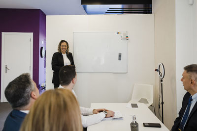 Happy businesswoman with colleagues sitting at desk in office meeting