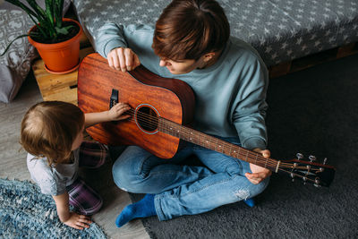 Little girl plays the guitar with her mother on the floor at home