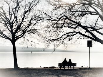 Rear view of silhouette man sitting on bench against sea