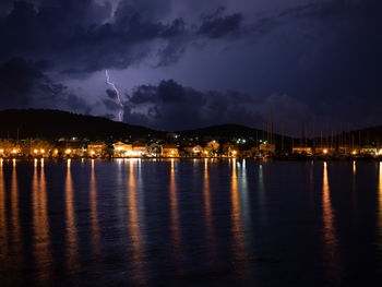 Illuminated city by sea against sky at night