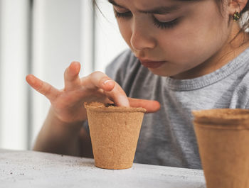 Caucasian girl planting seeds in a cardboard cup pushing her finger.