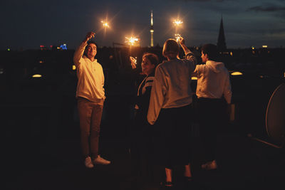Rear view of people standing on illuminated street at night