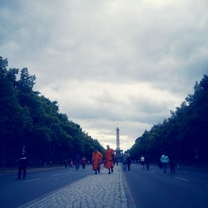 People walking on road against cloudy sky