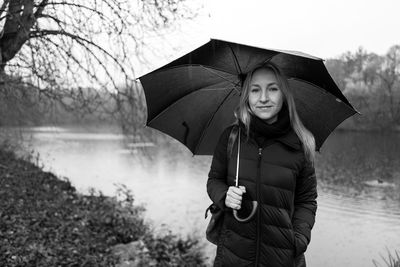 Portrait of smiling woman holding umbrella while standing against lake