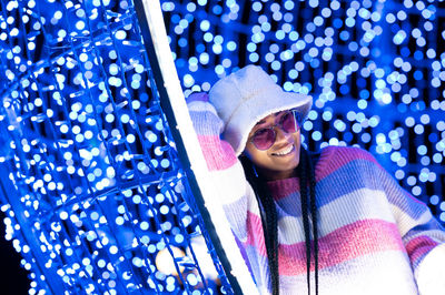 Joyful woman of color with a white beanie braided hairstyle and pink glasses enjoying the christmas 