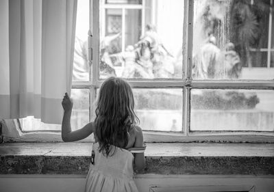 Rear view of girl looking through window at home