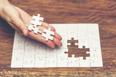 Cropped hand of woman playing jigsaw puzzle at table