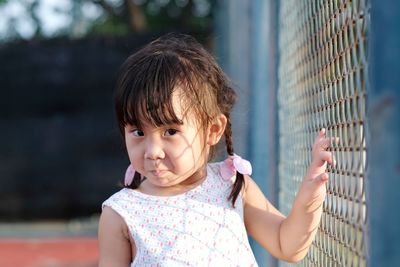 Portrait of cute girl touching chainlink fence