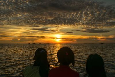Rear view of women looking at sea against sky during sunset