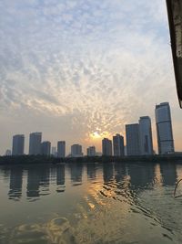 Sea by buildings against sky during sunset