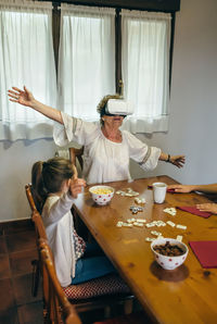 Senior woman wearing virtual reality headshot while sitting with granddaughter at table