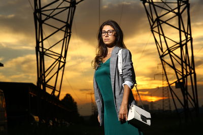 Portrait of young woman standing against sky during sunset