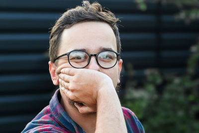 A portrait of a man in his 20s, wearing eyeglasses, with black hair styled neatly. stands outdoors